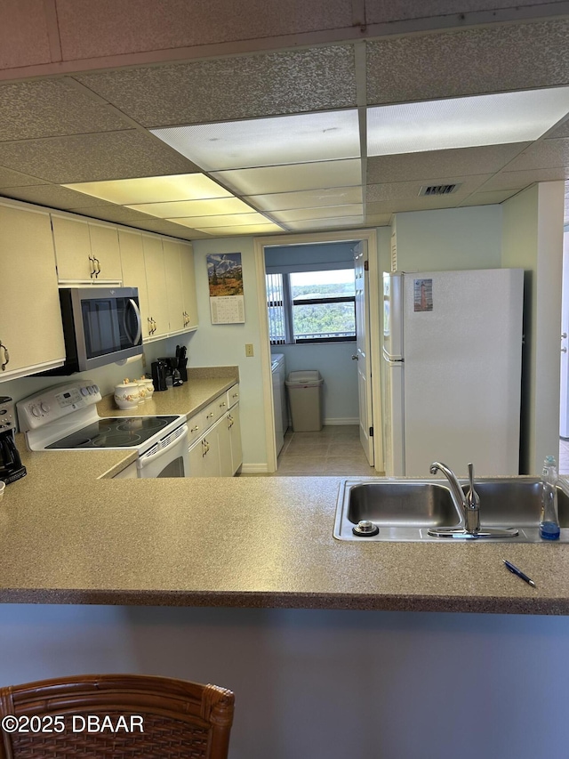 kitchen with a paneled ceiling, visible vents, a sink, and white appliances