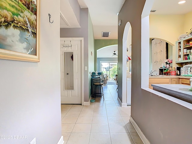 hallway with arched walkways, baseboards, visible vents, and light tile patterned flooring