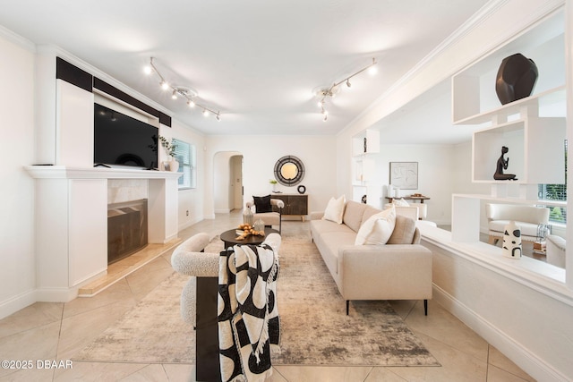 tiled living room with a high end fireplace, ornamental molding, and rail lighting