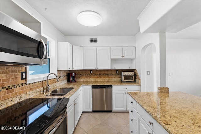 kitchen featuring white cabinetry, light stone countertops, stainless steel appliances, backsplash, and ornamental molding