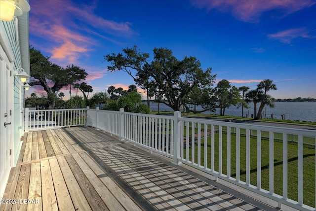 deck at dusk featuring a lawn and a water view