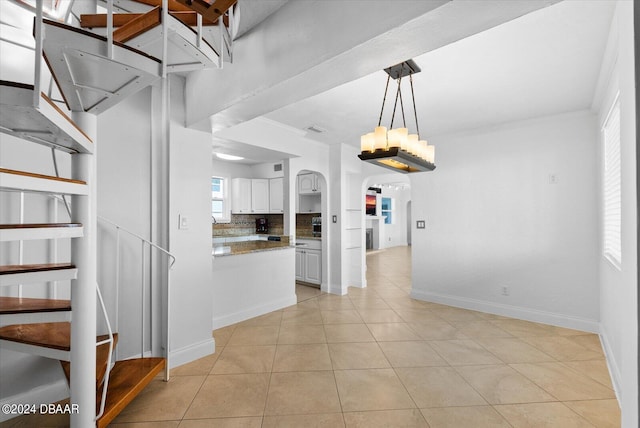 kitchen with hanging light fixtures, light tile patterned floors, tasteful backsplash, white cabinets, and ornamental molding