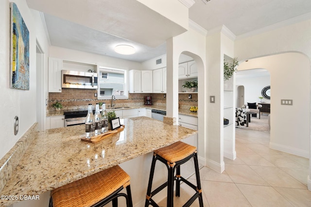 kitchen with sink, appliances with stainless steel finishes, a kitchen breakfast bar, light stone countertops, and white cabinets