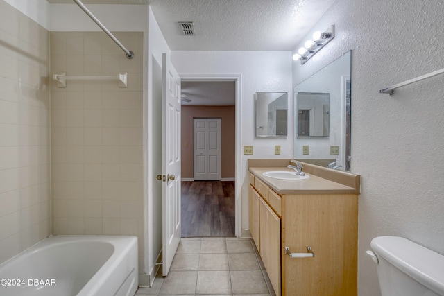 full bathroom with tiled shower / bath, a textured ceiling, vanity, tile patterned floors, and toilet