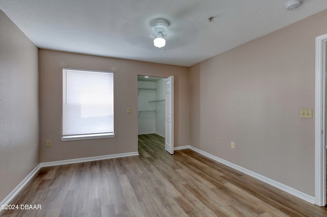 unfurnished bedroom featuring ceiling fan, light hardwood / wood-style flooring, and a walk in closet