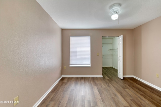 unfurnished bedroom with a closet, a spacious closet, hardwood / wood-style floors, and ceiling fan