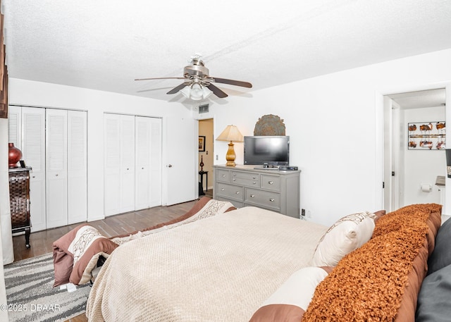 bedroom with multiple closets, wood-type flooring, ceiling fan, and a textured ceiling