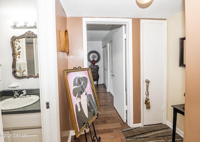 corridor with dark wood-type flooring, sink, and a textured ceiling