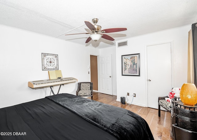 bedroom featuring a textured ceiling, light hardwood / wood-style flooring, ornamental molding, and ceiling fan