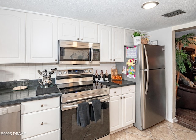 kitchen featuring appliances with stainless steel finishes, tasteful backsplash, white cabinets, light tile patterned floors, and a textured ceiling