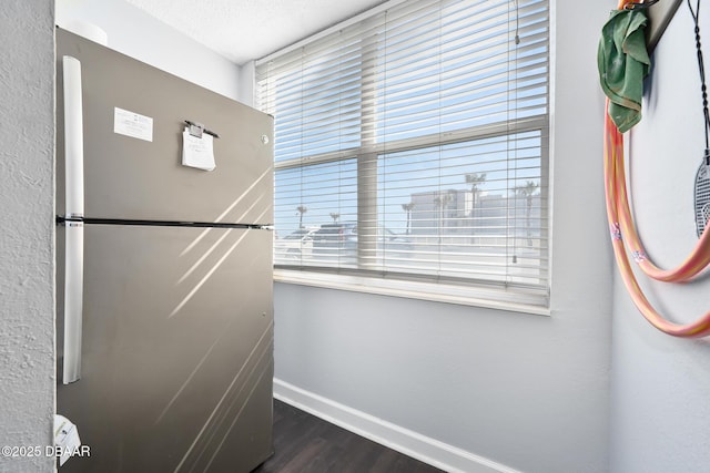 interior space with freestanding refrigerator, a textured ceiling, baseboards, and wood finished floors