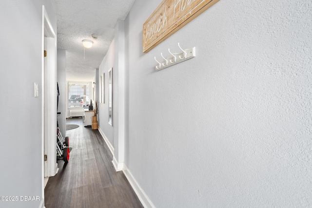 hall featuring dark wood-type flooring, a textured ceiling, and baseboards