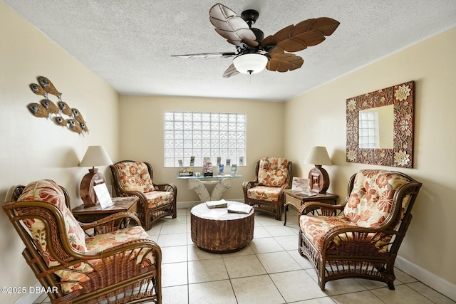 living area featuring light tile patterned flooring, ceiling fan, a textured ceiling, and baseboards