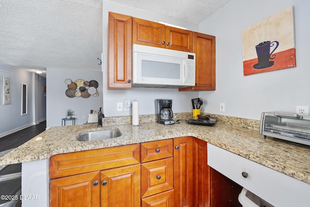 kitchen featuring a textured ceiling, white microwave, a peninsula, a sink, and brown cabinets