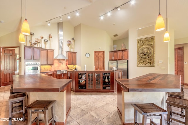 kitchen featuring stainless steel appliances, track lighting, high vaulted ceiling, pendant lighting, and wall chimney exhaust hood