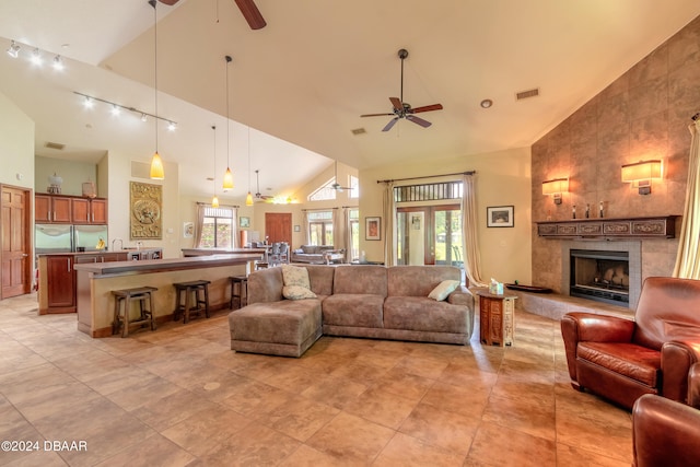 tiled living room with high vaulted ceiling, a tiled fireplace, and ceiling fan