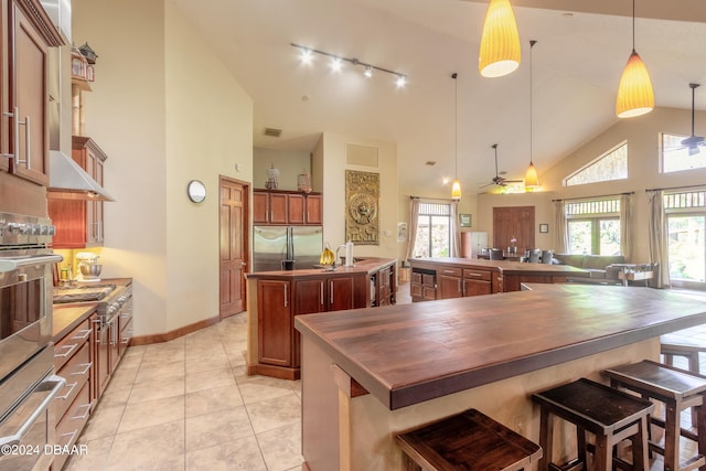 kitchen featuring stainless steel refrigerator, ceiling fan, high vaulted ceiling, hanging light fixtures, and a kitchen island