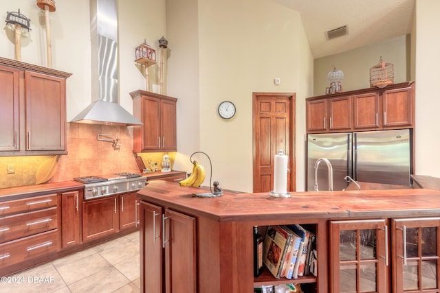 kitchen with wall chimney range hood, appliances with stainless steel finishes, light tile patterned floors, decorative backsplash, and vaulted ceiling