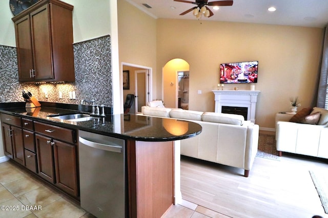 kitchen with dark brown cabinetry, sink, dark stone countertops, stainless steel dishwasher, and backsplash