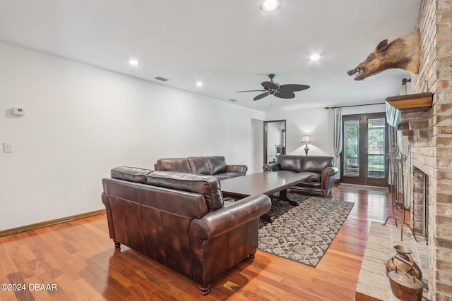 living room featuring hardwood / wood-style floors, ceiling fan, and a brick fireplace