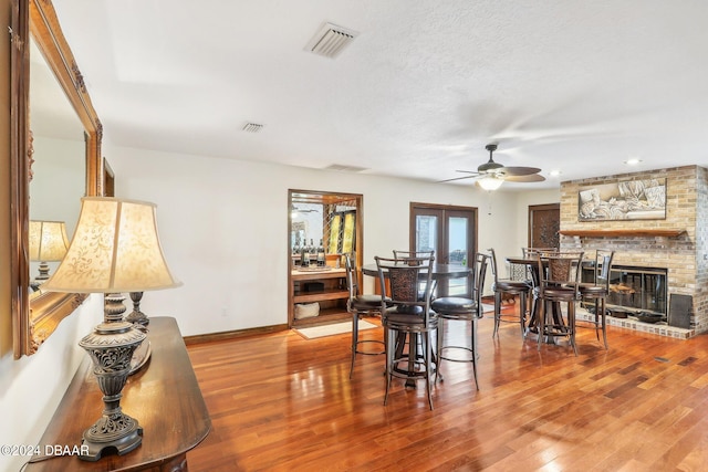 dining space featuring a textured ceiling, wood-type flooring, ceiling fan, and a brick fireplace