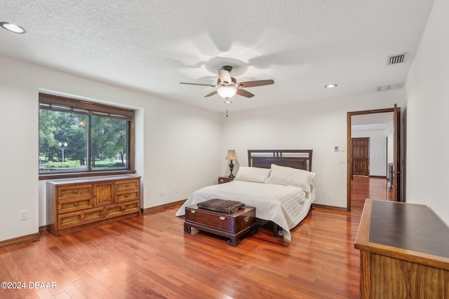 bedroom with a textured ceiling, light wood-type flooring, and ceiling fan