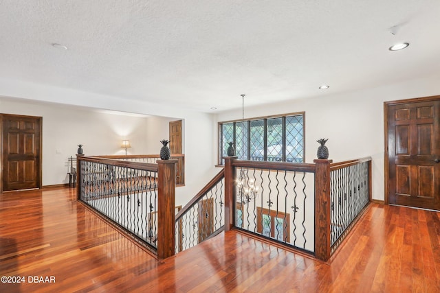 hall with hardwood / wood-style flooring, a textured ceiling, and a notable chandelier