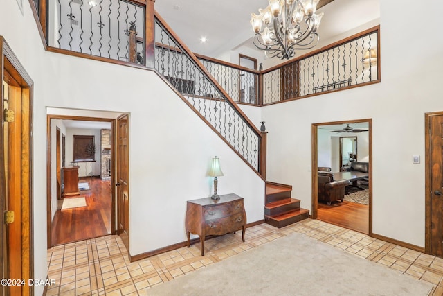 foyer featuring a towering ceiling, ceiling fan with notable chandelier, and light wood-type flooring