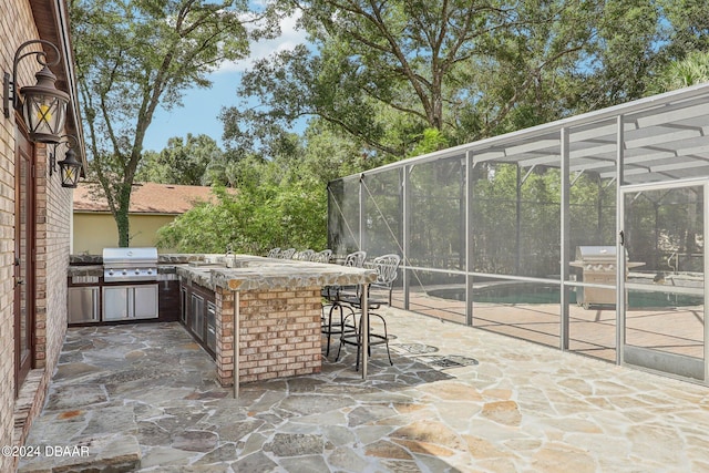 view of patio with a bar, a grill, glass enclosure, and exterior kitchen