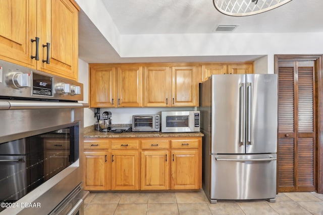 kitchen with stainless steel appliances, light tile patterned flooring, and stone counters