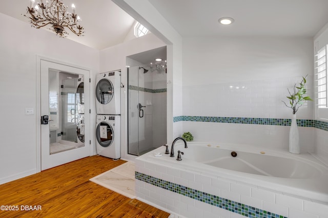 bathroom featuring a chandelier, stacked washer and dryer, a stall shower, a garden tub, and wood finished floors