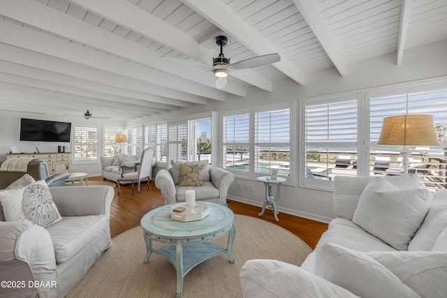 living area with baseboards, wood finished floors, a ceiling fan, and beam ceiling