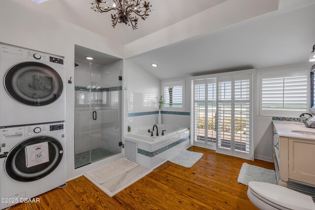 full bath featuring a chandelier, a shower stall, a garden tub, stacked washer / dryer, and wood finished floors