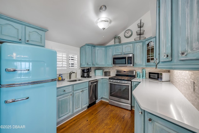 kitchen featuring light countertops, a sink, backsplash, appliances with stainless steel finishes, and dark wood finished floors