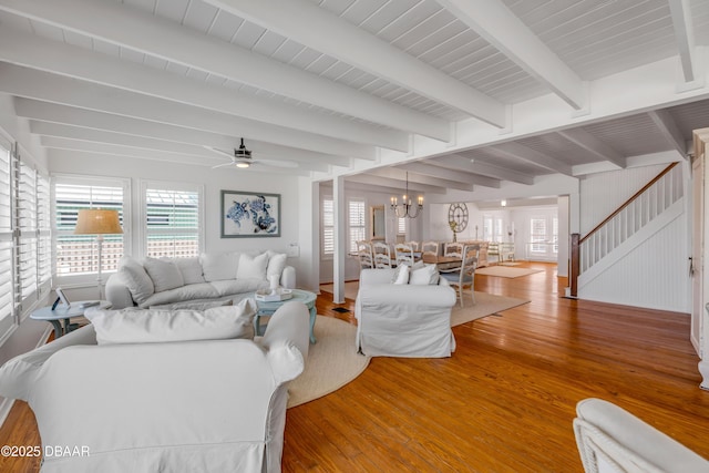 living area featuring stairs, wood finished floors, beam ceiling, and ceiling fan with notable chandelier