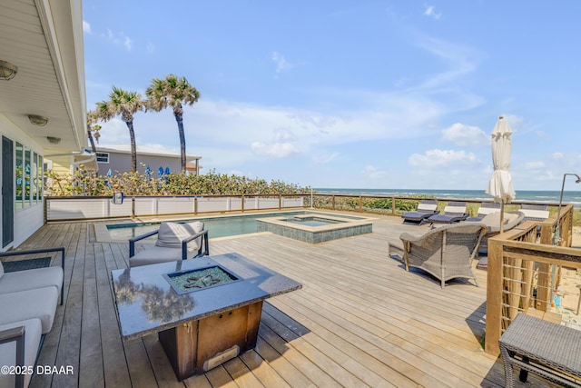 wooden deck featuring a fire pit, a pool with connected hot tub, and a water view