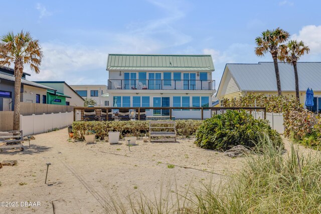 back of property with a balcony, metal roof, fence, and a standing seam roof