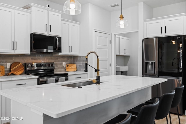 kitchen featuring a kitchen island with sink, white cabinets, sink, decorative light fixtures, and stainless steel appliances