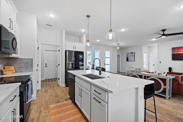 kitchen with a kitchen island with sink, black appliances, sink, light hardwood / wood-style flooring, and white cabinetry