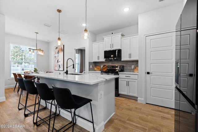 kitchen with a kitchen island with sink, stainless steel electric stove, sink, hanging light fixtures, and white cabinetry