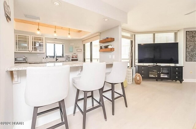 kitchen with white cabinets, kitchen peninsula, a breakfast bar area, tasteful backsplash, and light stone countertops