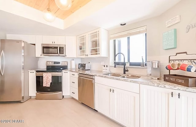 kitchen with white cabinets, stainless steel appliances, sink, and light stone countertops