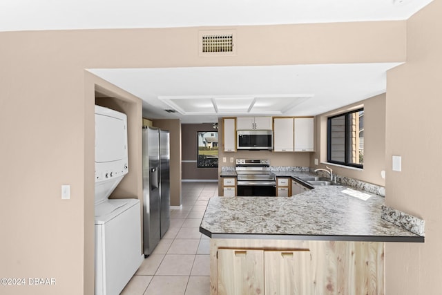 kitchen featuring sink, light tile patterned floors, appliances with stainless steel finishes, stacked washer / drying machine, and kitchen peninsula