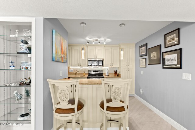 kitchen featuring stainless steel appliances, sink, cream cabinets, a breakfast bar area, and pendant lighting