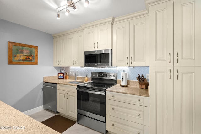 kitchen featuring tasteful backsplash, appliances with stainless steel finishes, light stone countertops, sink, and cream cabinetry