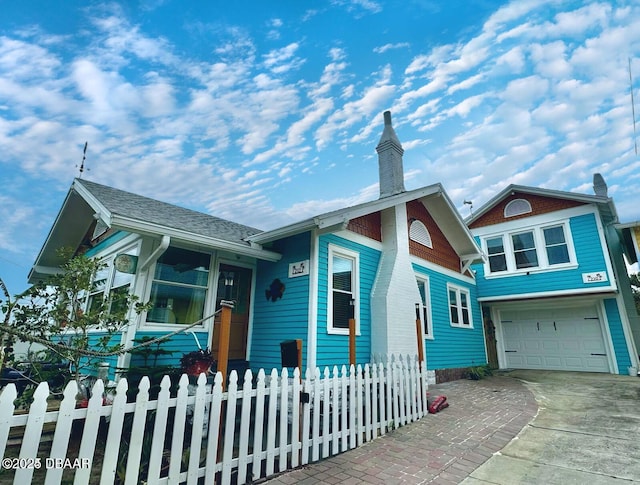 view of front of house with a shingled roof, a chimney, concrete driveway, a garage, and a fenced front yard