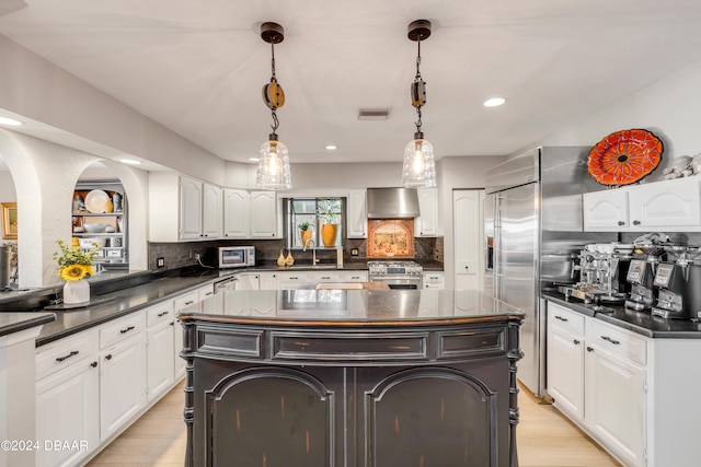 kitchen featuring stainless steel appliances, white cabinetry, hanging light fixtures, a center island, and wall chimney range hood