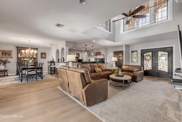 living room with a towering ceiling, ceiling fan with notable chandelier, light hardwood / wood-style flooring, and french doors