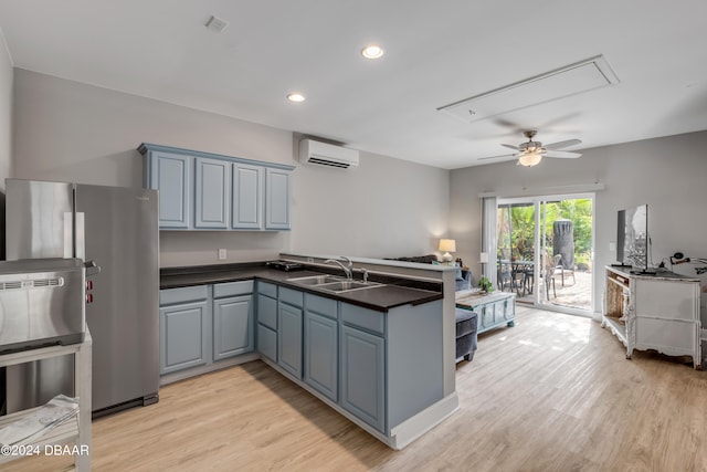 kitchen with light hardwood / wood-style floors, kitchen peninsula, sink, stainless steel refrigerator, and a wall mounted air conditioner