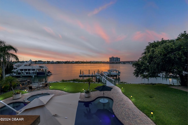 patio terrace at dusk featuring a water view, a lawn, and a boat dock